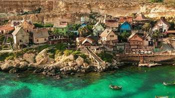Sprachreisen Malta Aufnahme eines Ausschnitts Maltas aus der Luft. Zu sehen ist ein Dorf direkt am Meer umgeben von türkisblauem Wasser.