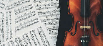 Musik Das Bild gleidert sich in zwei Abschnitte. Auf der linken Seite befinden sich mehrere Notenblätter, welche durcheinander liegen und sich überlappen. Auf der rechten Seite neben den Blättern liegt eine Geige aus dunklem Holz.