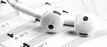 Musikwissenschaft Das Bild zeigt eine Nahaufnahme von einem Notenblatt, auf dem In-ear-Kopfhörer liegen. Das Notenblatt sowie die Kopfhörer haben eine weiße Farbe.